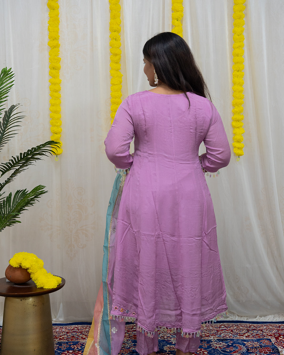 Woman in a pink dress standing in front of a white curtain with yellow decorative elements. laaki