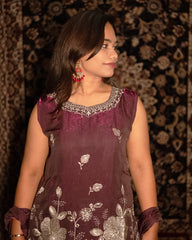Woman wearing a maroon traditional outfit with silver embroidery against a patterned background laaki.