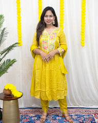 laaki Woman in a yellow traditional outfit standing in front of a white curtain with yellow decorations.
