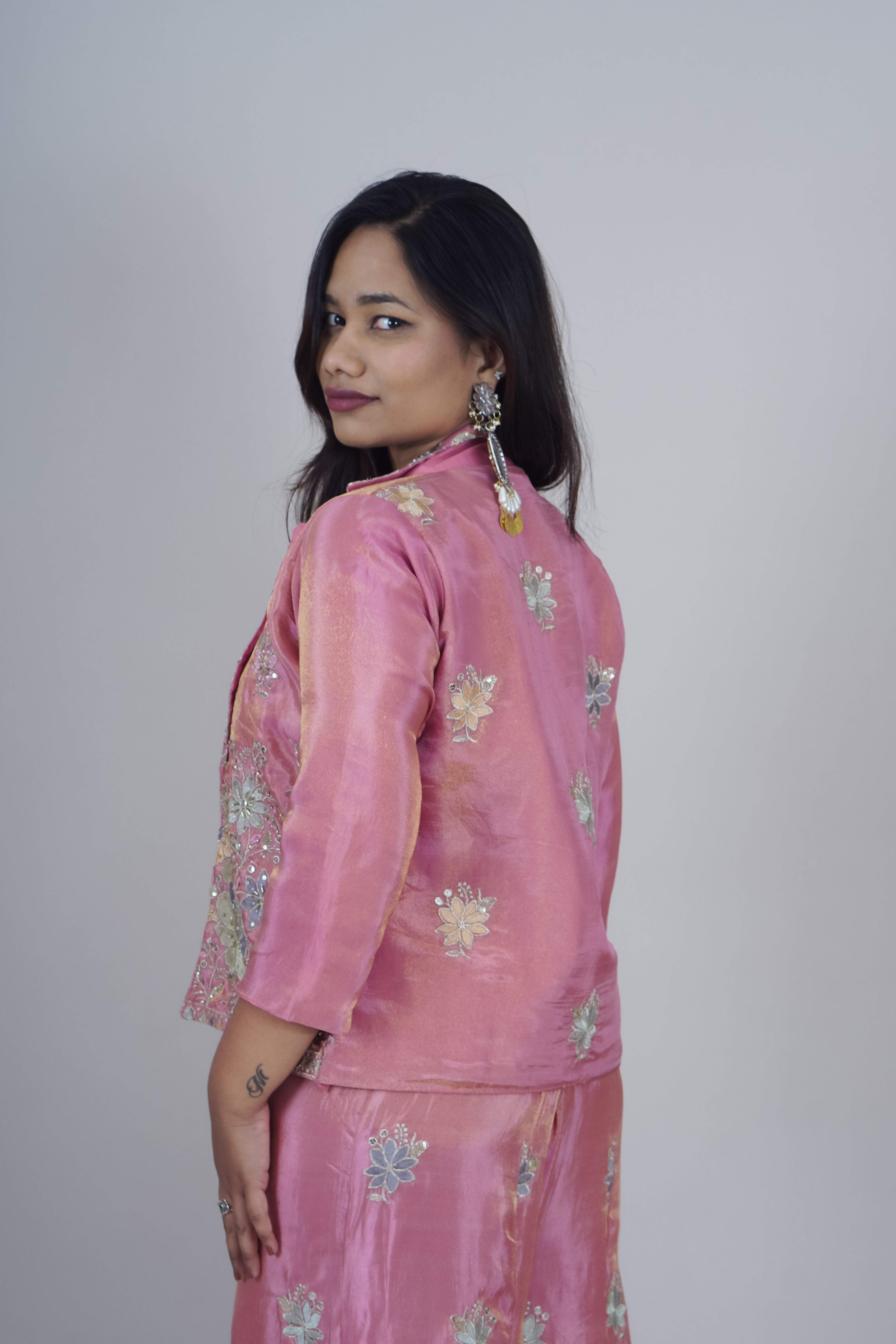 Woman wearing a pink traditional outfit with floral patterns on a plain background