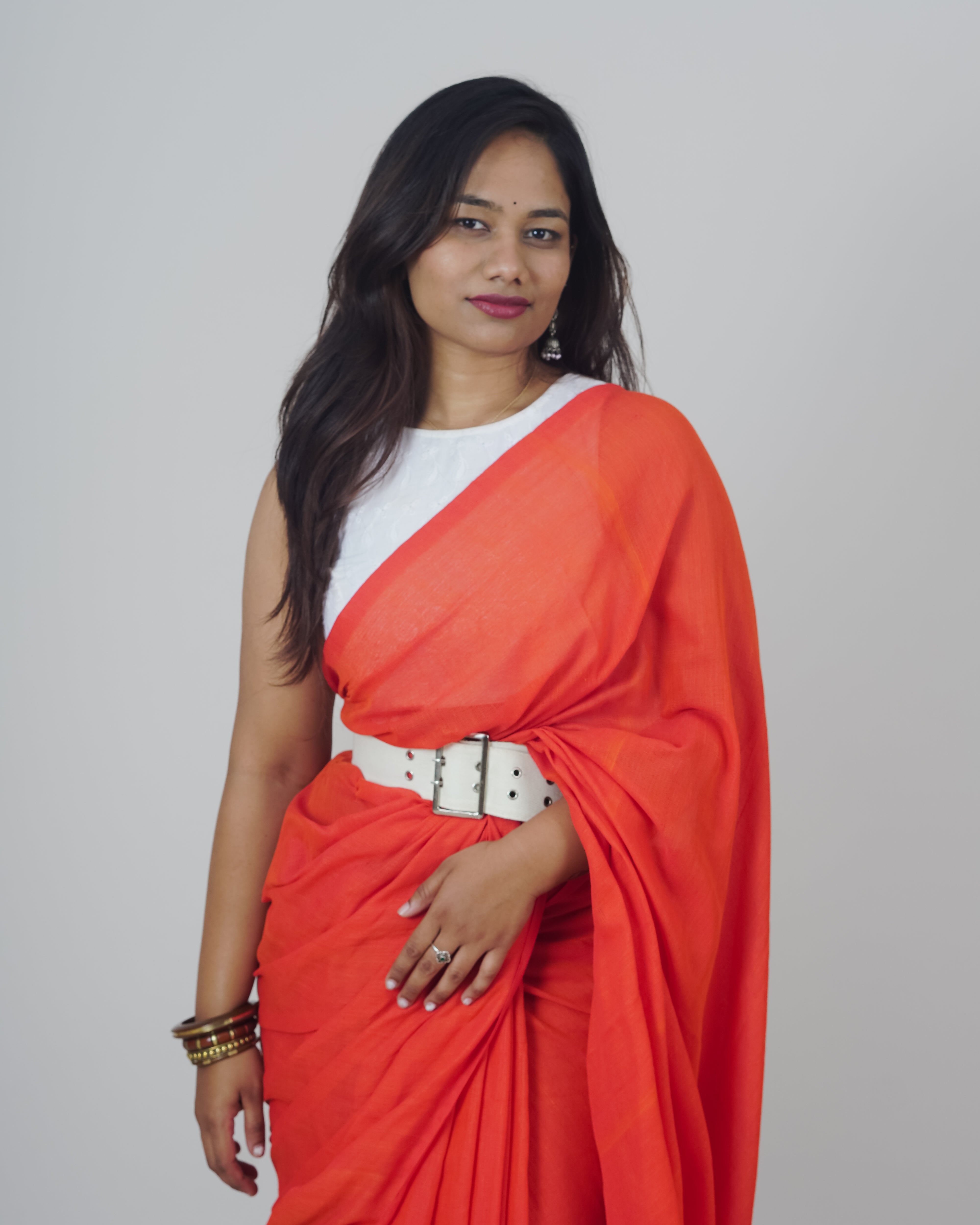 Woman wearing a bright red saree with a white blouse against a plain background