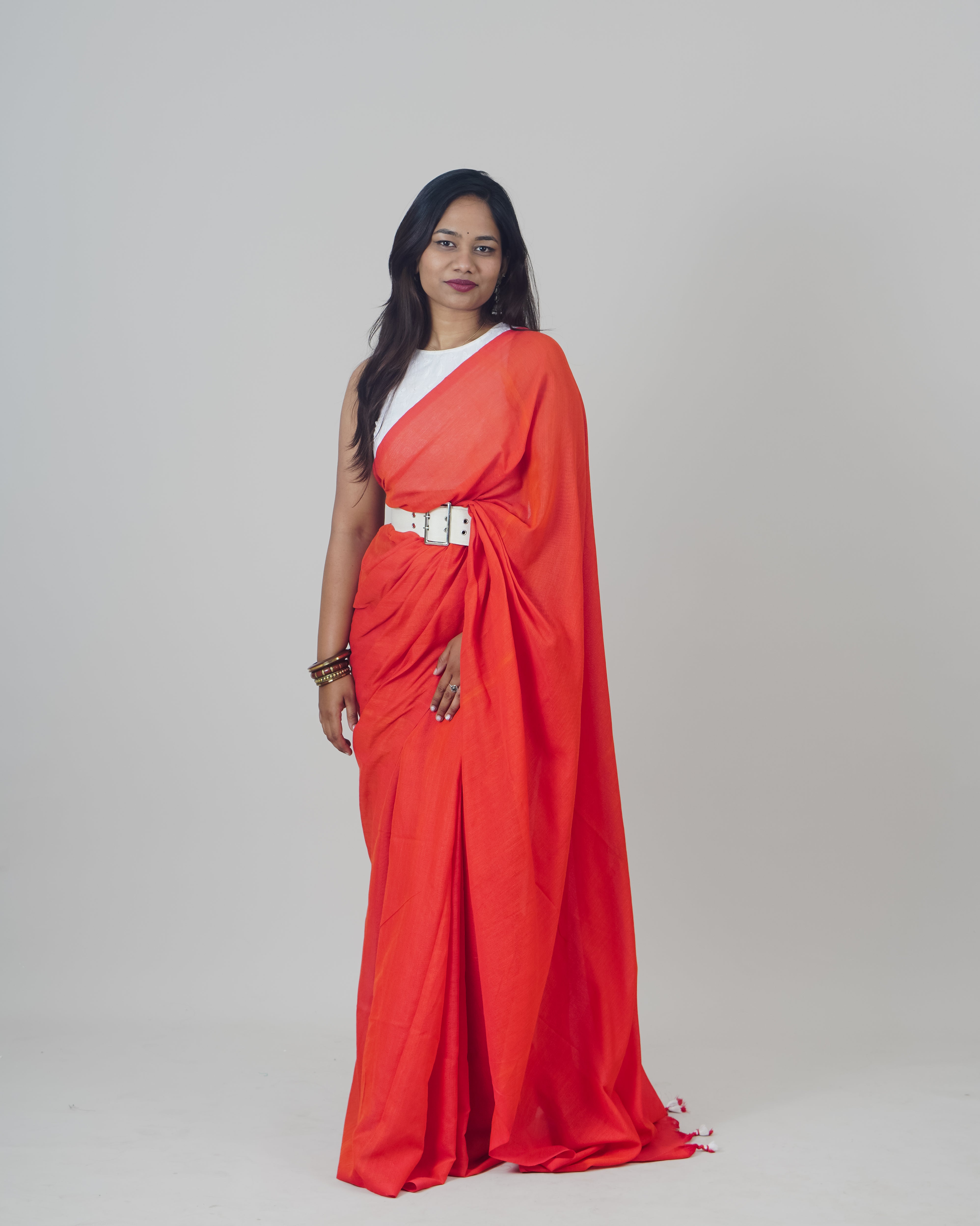 Woman wearing a red saree with a white blouse against a plain background  laaki.co