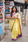 Woman in a yellow saree with purple border walking past bookstacks.www.laaki.co