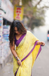Woman in a yellow saree with purple border walking on a street. www.laaki.co