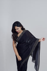 Woman wearing a black saree with gold border against a plain background www.laaki.co