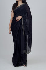 Woman wearing a black saree with silver border on a plain background