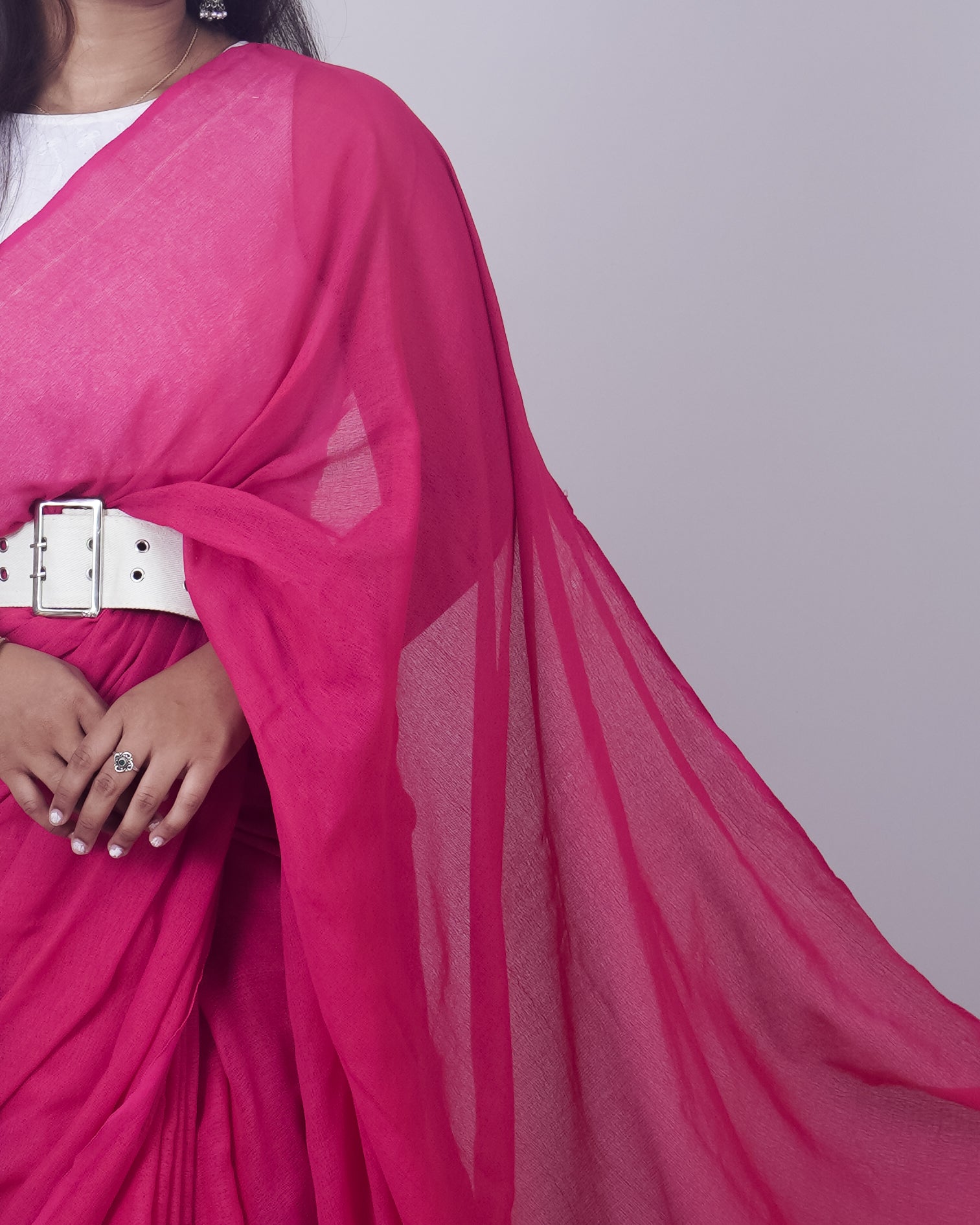 Person wearing a bright pink saree with a white belt on a light gray background