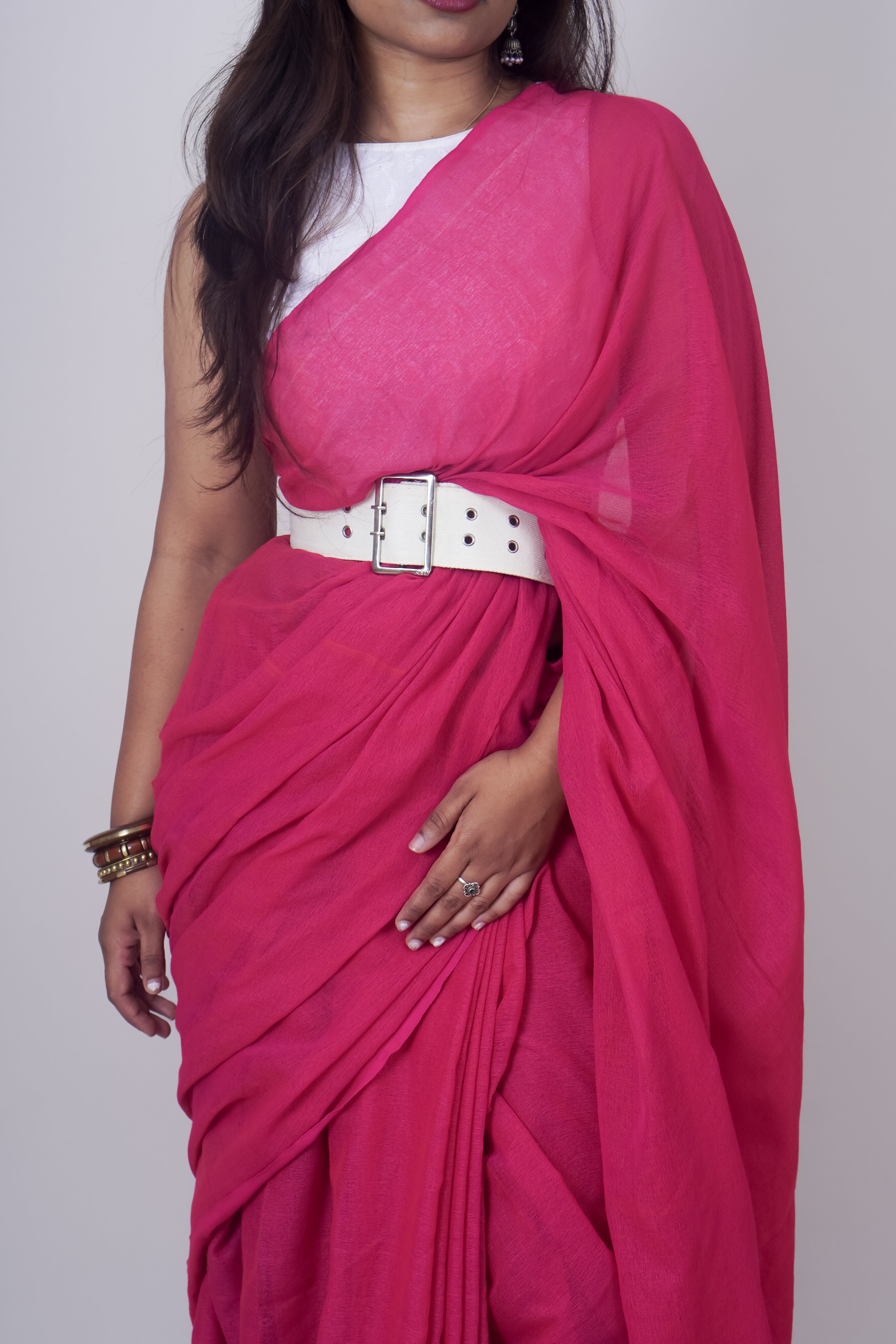 Woman wearing a bright pink saree with a white belt on a plain background