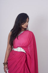 Woman wearing a bright pink saree with a white belt on a plain background