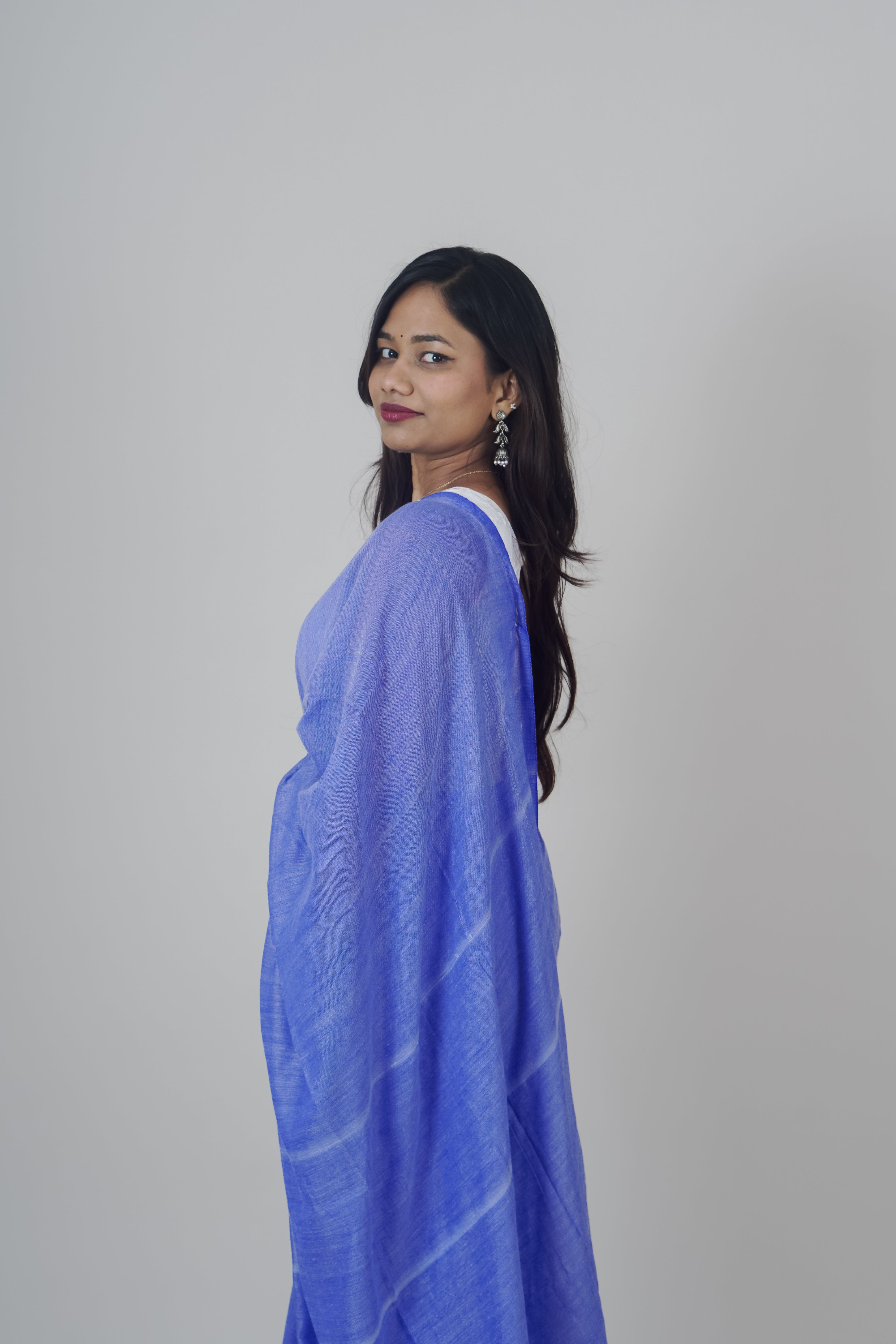 Woman wearing a blue saree with white patterns on a gray background