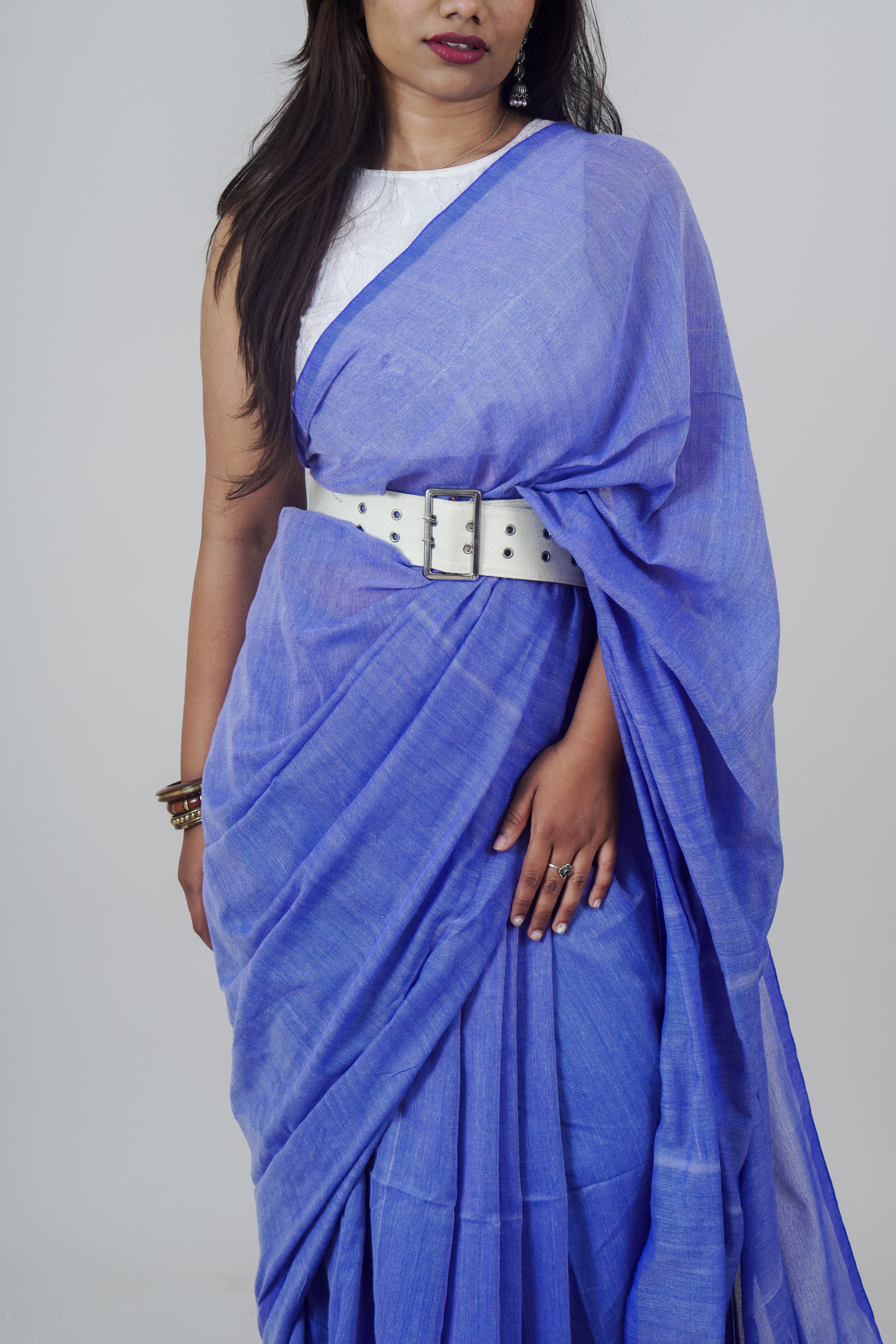 Woman wearing a blue saree with a white belt on a gray background