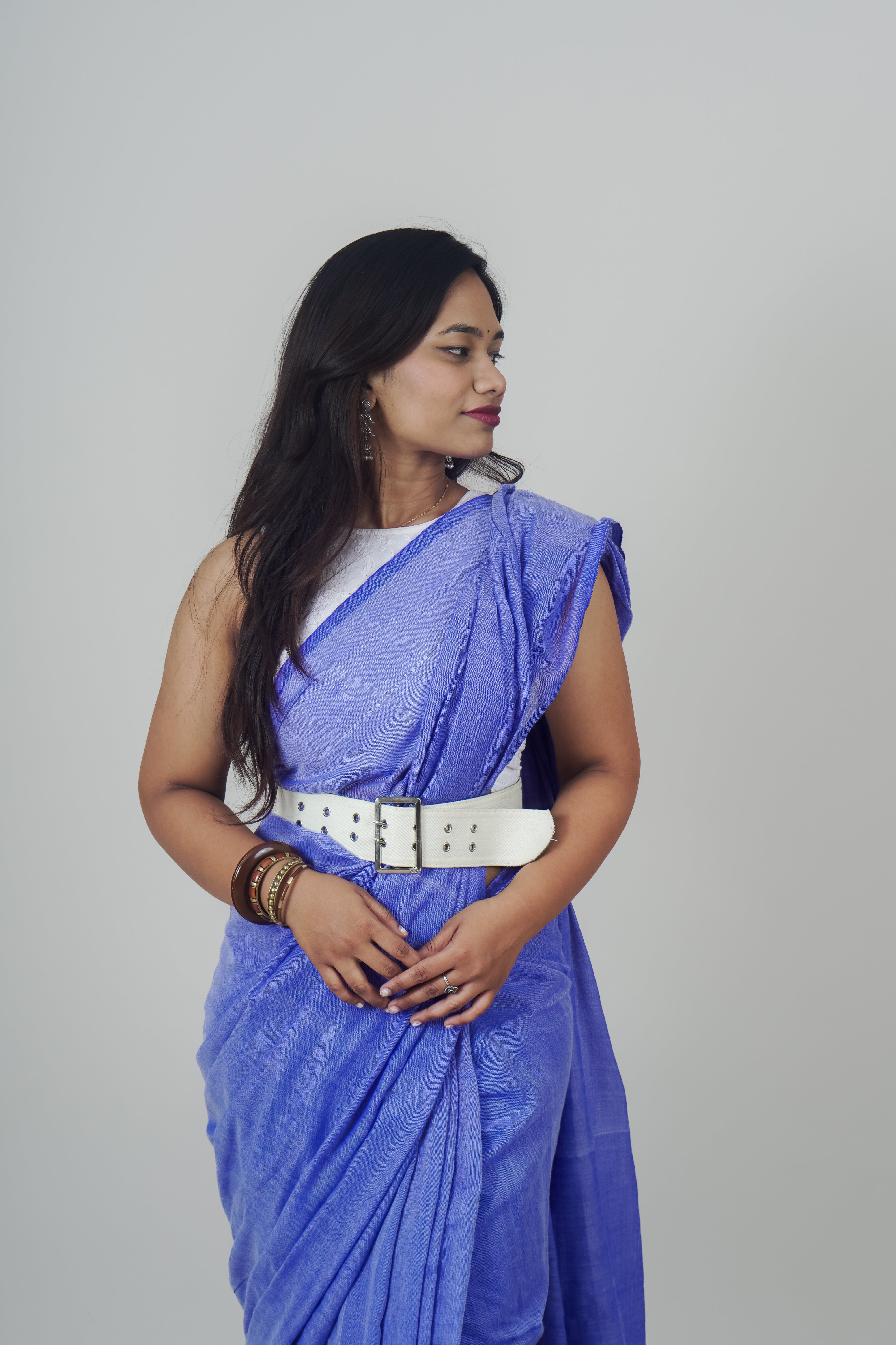 Woman wearing a blue saree with a white belt on a gray background