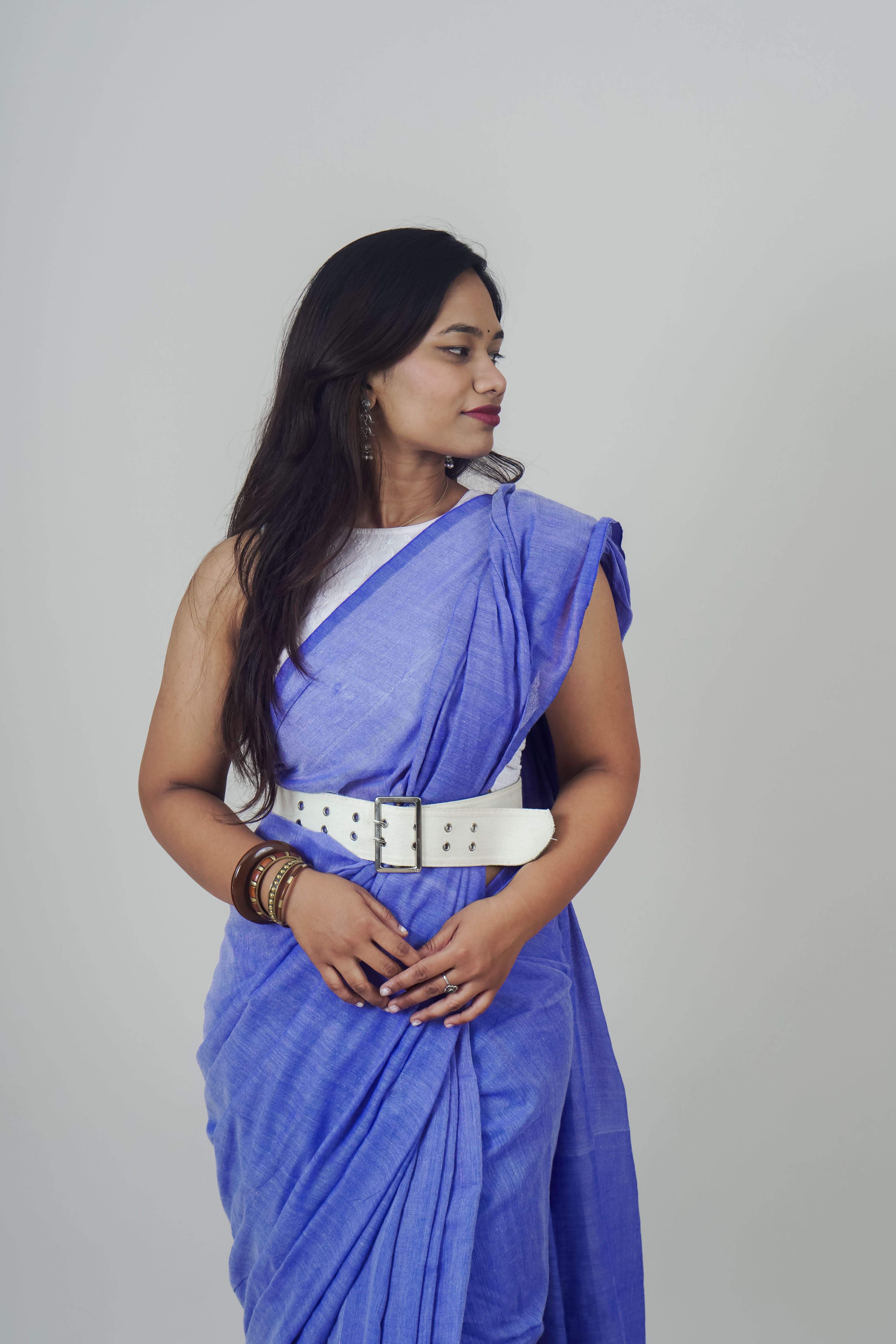 Woman wearing a blue saree with a white belt on a gray background
