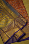 Close-up of a saree with gold, purple, and orange patterns on a wooden surface.