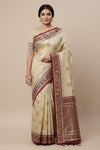 Woman wearing a beige saree with red and brown border on a beige background