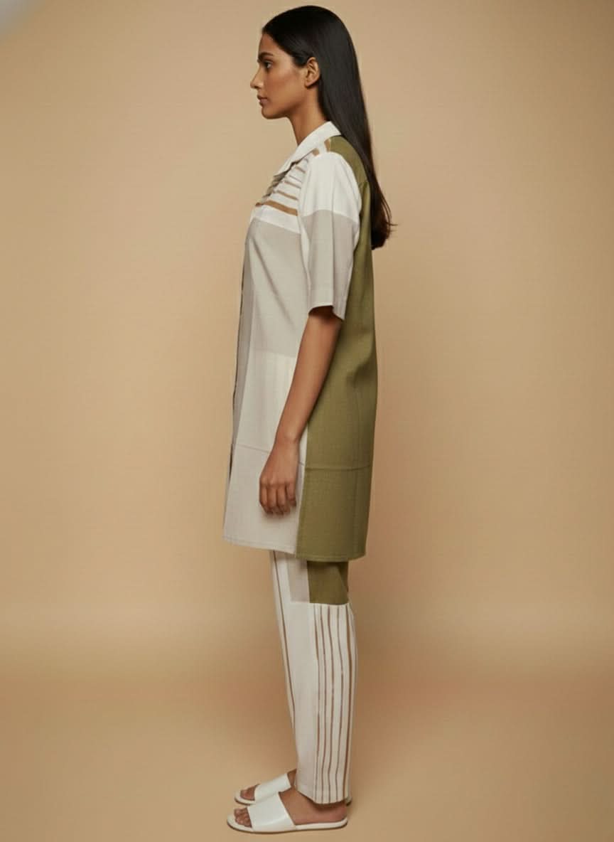 laaki Woman wearing a white shirt and green apron with beige pants against a beige background