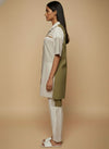 laaki Woman wearing a white shirt and green apron with beige pants against a beige background