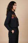 Woman wearing a black embroidered shirt and pants against a beige www.laaki.co background