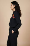 Woman wearing a black outfit with floral embroidery on a beige background. www.laaki.co