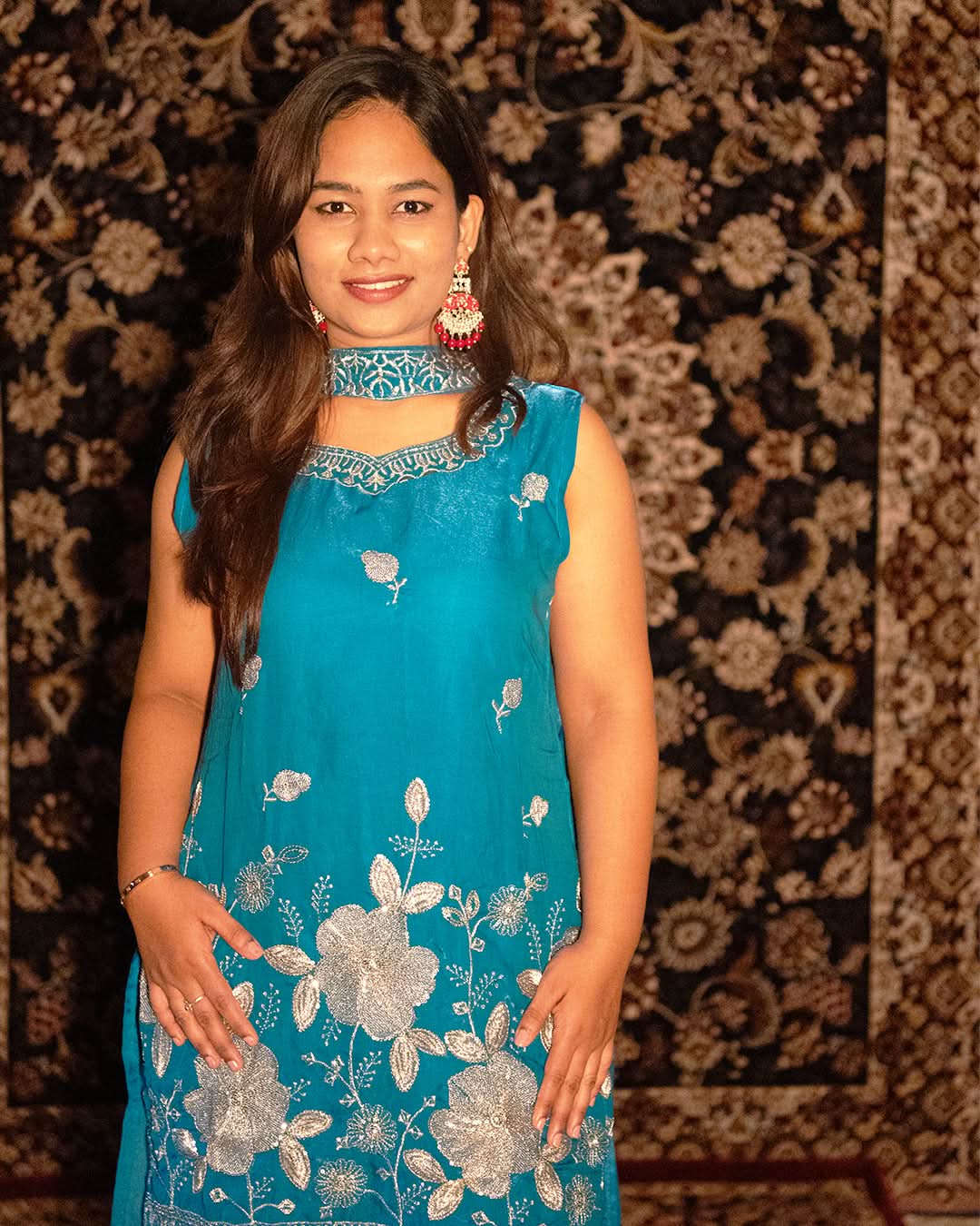 laaki Woman wearing a blue dress with floral patterns against a patterned wall.