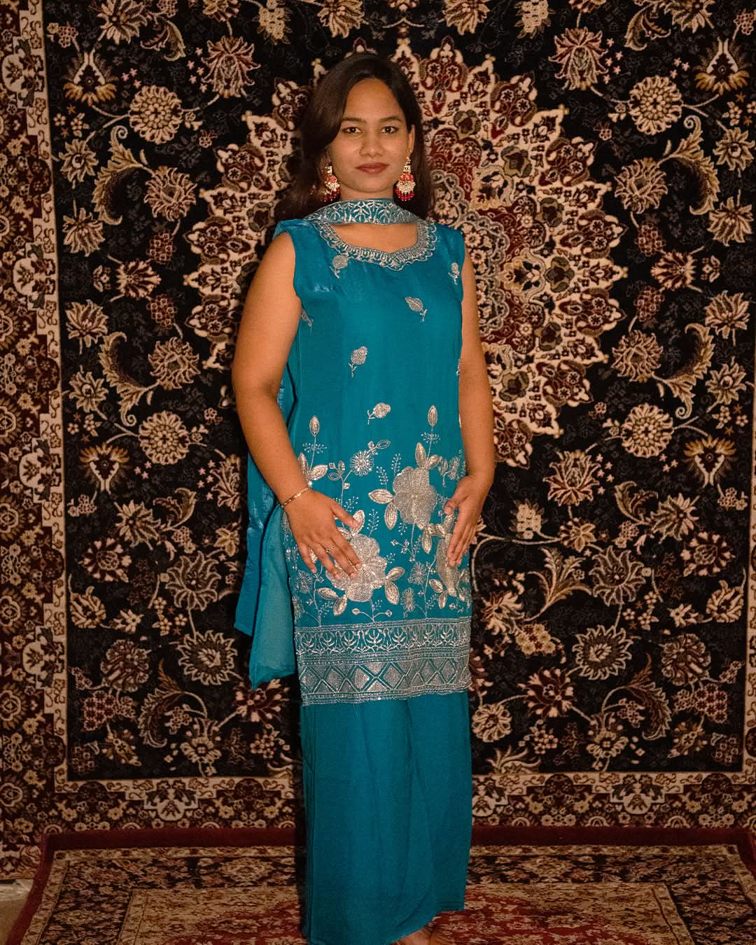 laaki Woman in a blue traditional outfit standing against a patterned wall.