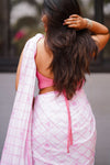 Woman wearing a pink saree with a white checkered pattern, standing outdoors.