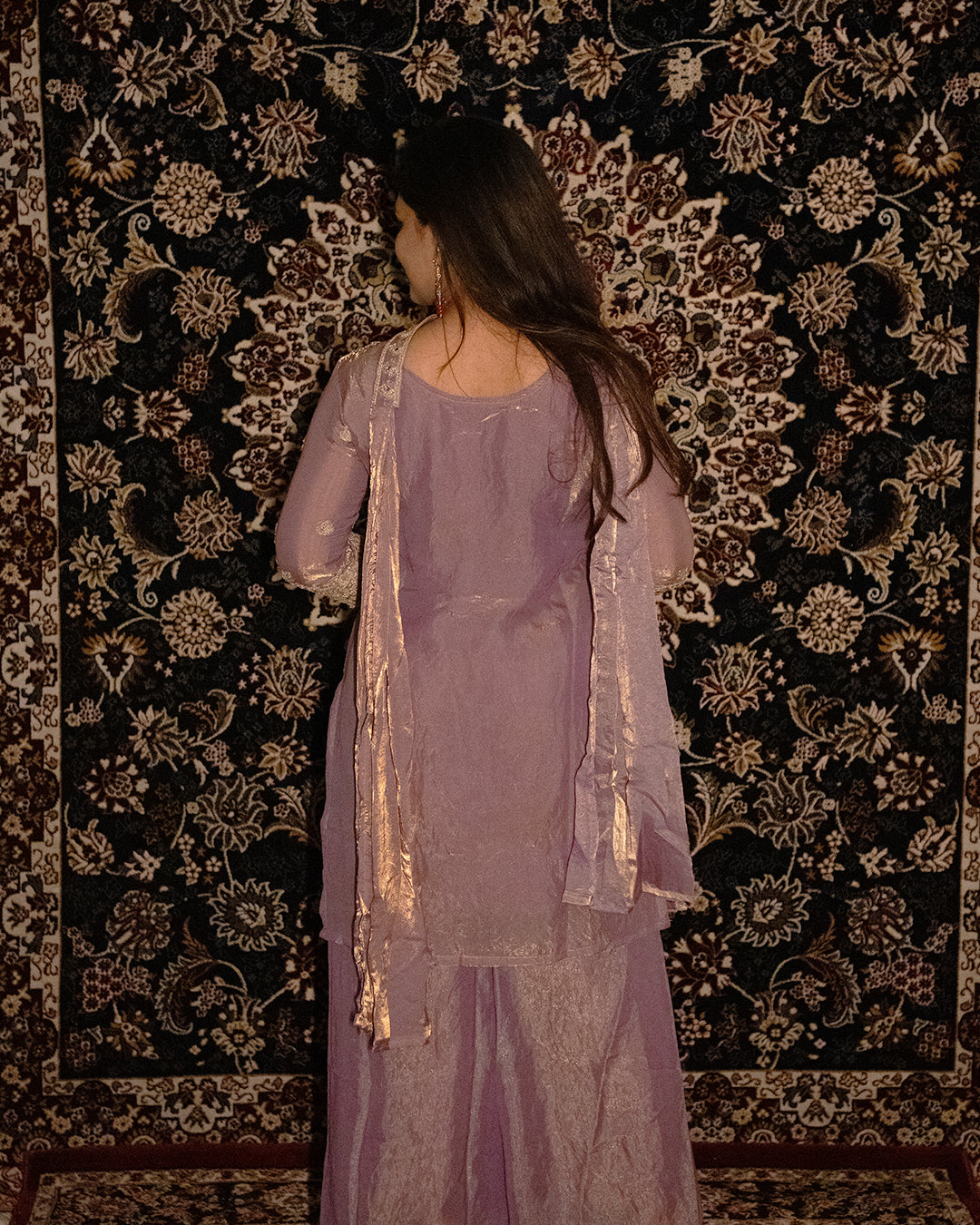 Woman in a lavender outfit standing against a patterned wall. sharas