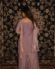 Woman in a lavender outfit standing against a patterned wall. sharas