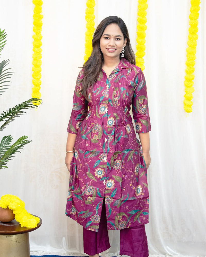 Woman wearing a magenta floral kurta with purple pants against a white background with yellow decorative elements. laaki