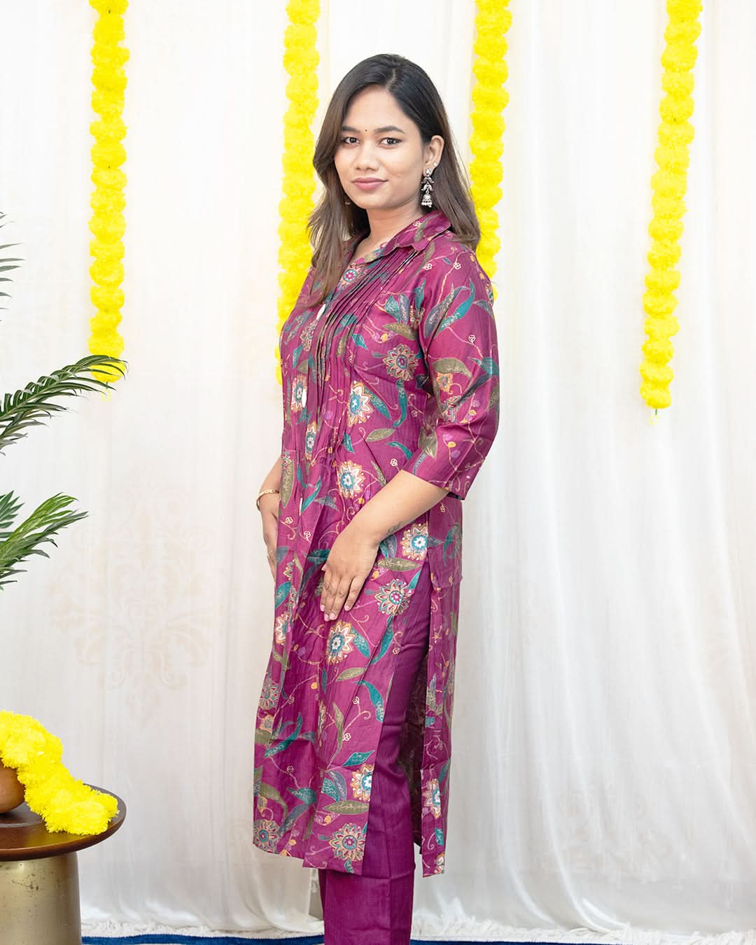 Woman wearing a pink floral kurta with pants against a white background with yellow decorations. laaki