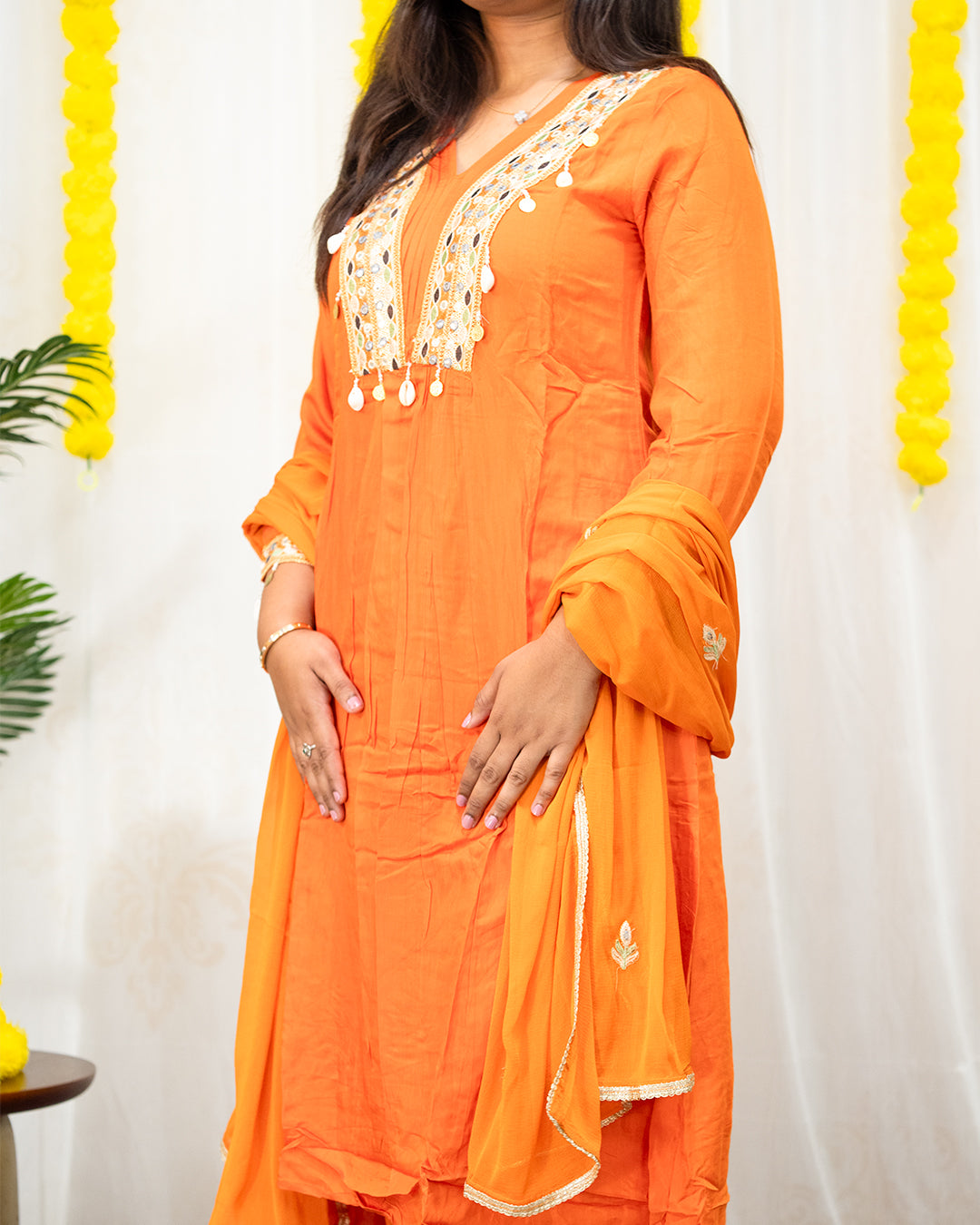 laaki Person wearing an orange traditional outfit with white embroidery against a white background.