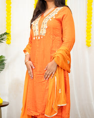laaki Person wearing an orange traditional outfit with white embroidery against a white background.