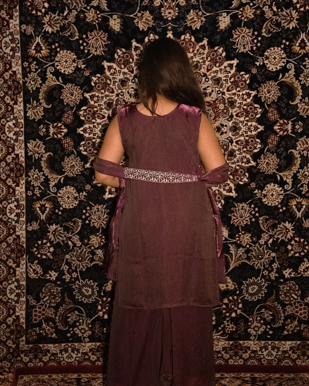 Person wearing a maroon traditional outfit with a patterned background