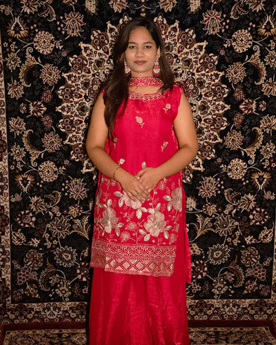 Woman wearing a pink traditional outfit with intricate patterns against a decorative black and gold background. laaki