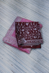 Two fabric items, one pink with lace details and one maroon with white floral patterns, on a textured surface.