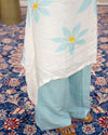 Person wearing a light blue outfit with a white shawl featuring blue floral patterns on a patterned rug. www.laaki.co