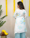 Woman wearing a white kurta with blue floral patterns against a decorative curtain background. www.laaki.co