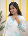 Woman wearing a white top with blue floral patterns and yellow accents, standing against a light background. www.laaki.co
