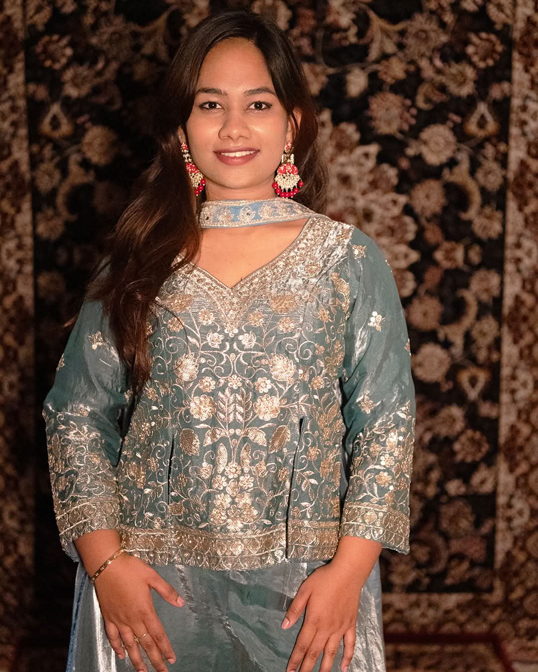 Woman wearing a traditional outfit with intricate patterns against a patterned background laaki