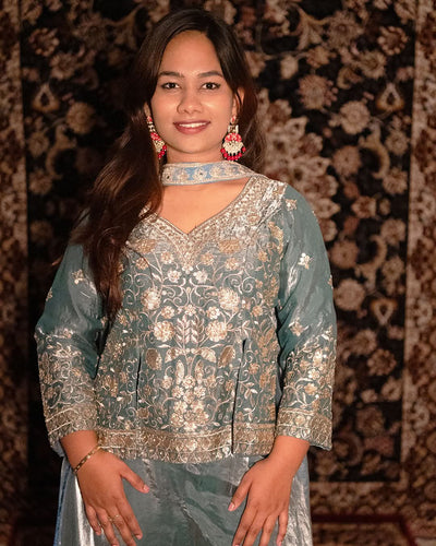 Woman wearing a traditional outfit with intricate patterns against a patterned background laaki