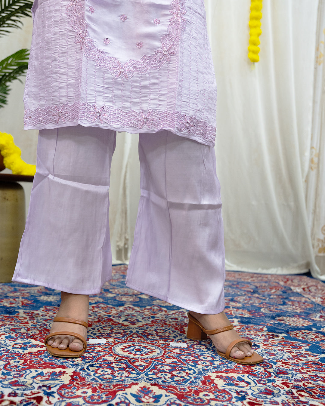 Person wearing a light purple outfit with floral embroidery on a patterned rug. www.laaki.co